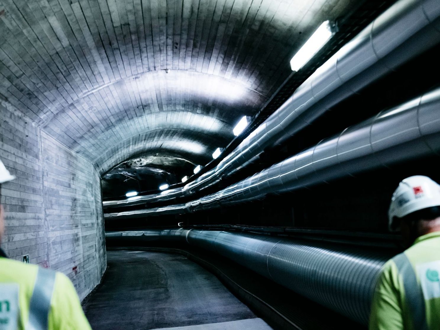 fjernvarmestyring: to arbeidere går gjennom en opplyst tunnel med tre store rør for fjernvarme
